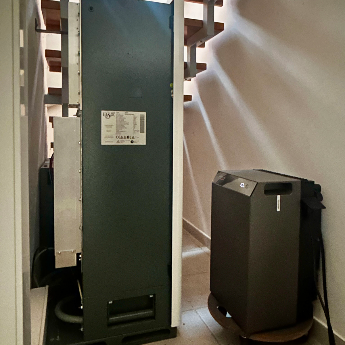 Achter deze netwerkkast heb ik de STREAM AC 5000 weggewerkt. Door de opening is hij vanaf de zijkant nog zichtbaar.
Onder de trap, naast de hoofdaccu, neemt hij nauwelijks extra ruimte in. Tegelijkertijd dient de STREAM AC 5000 als UPS voor de serverkast.
Naast de serverkast voorziet hij ’s nachts ook het basisverbruik van het huis van stroom, totdat het ingestelde minimale back-upniveau is bereikt.